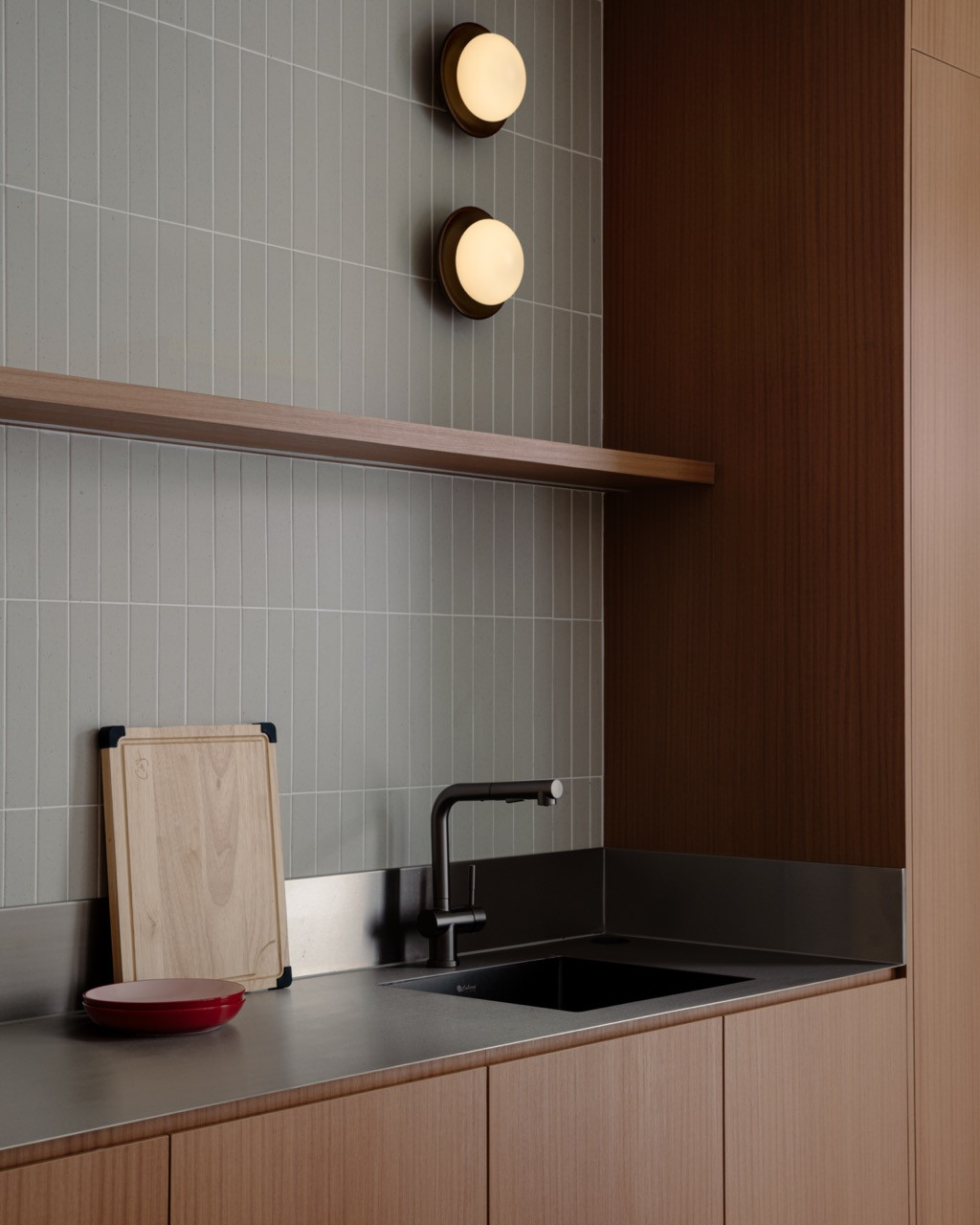 The dry kitchen has a pale tiled wall, a single open shelf and a stainless steel worktop