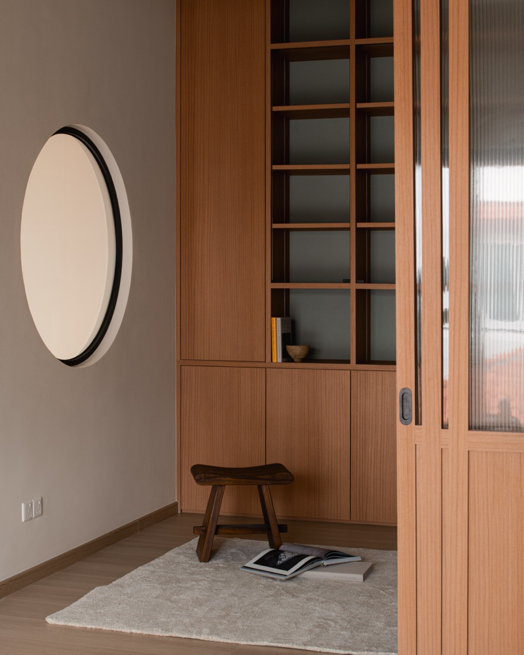 Reeded-glass sliding doors open onto a reading corner with built-in shelving and a round wall feature