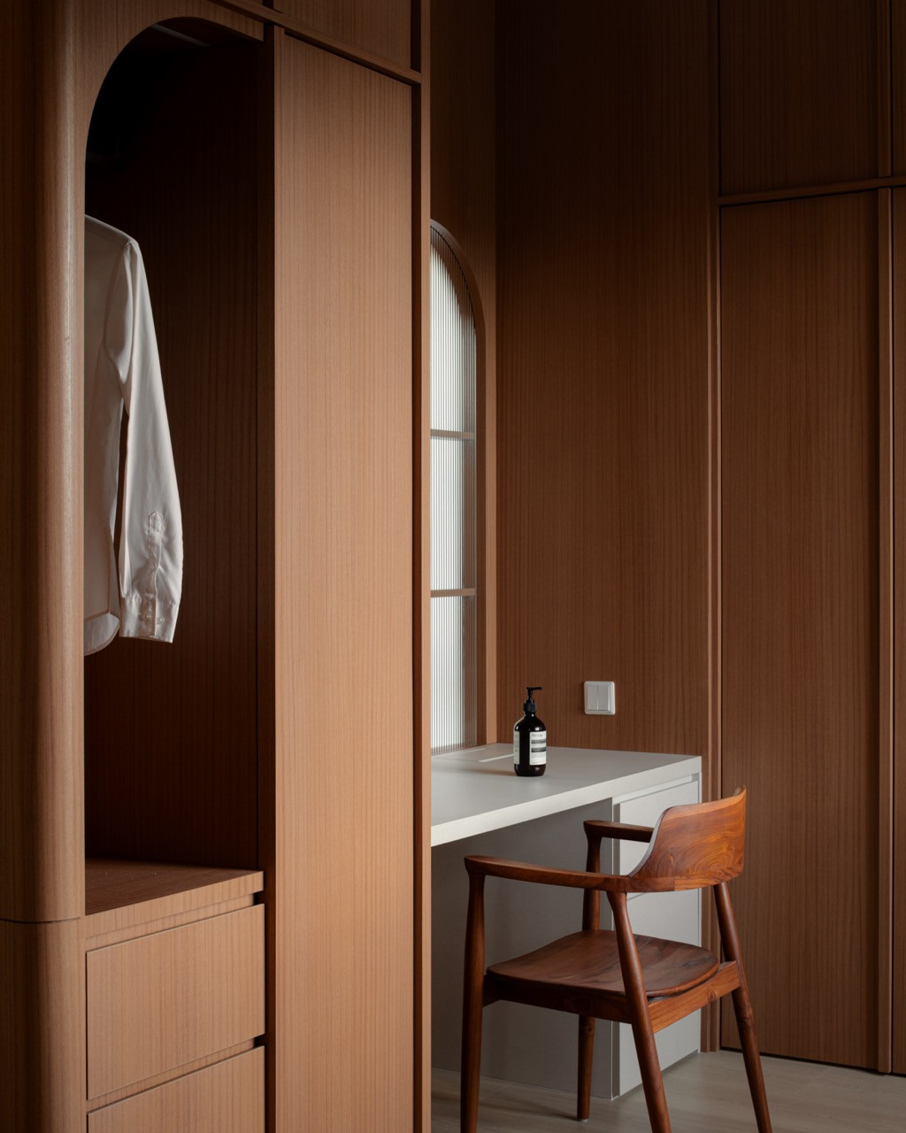 The dressing area pairs arched hanging space with a built-in desk and a reeded-glass window