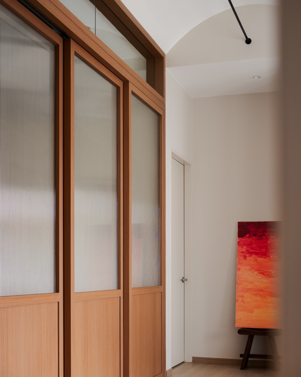 Sliding doors in wood-look laminate and reeded glass line an upstairs corridor, where the abstract painting Sunset, by CX Soon, rests on a stool
