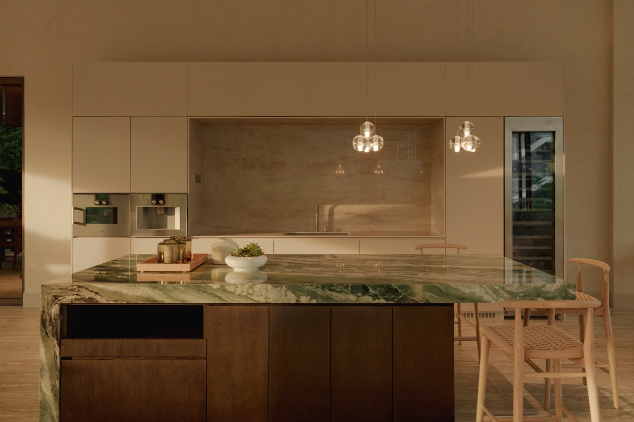 The kitchen island is topped in a green stone with a waterfall edge against dark wood cabinetry