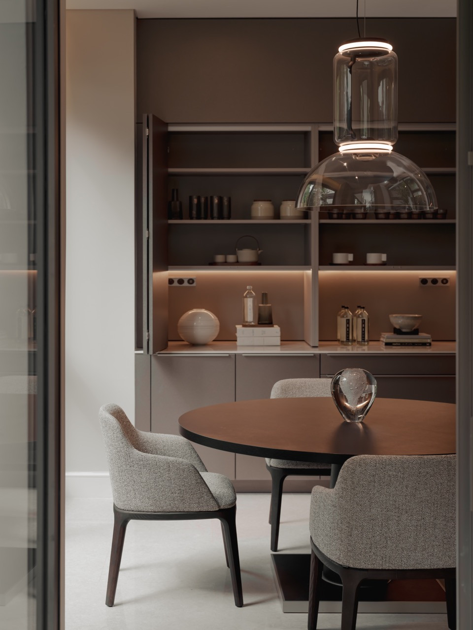 Sleek, neutral tones define the dining nook, with an open cabinet beside the round table