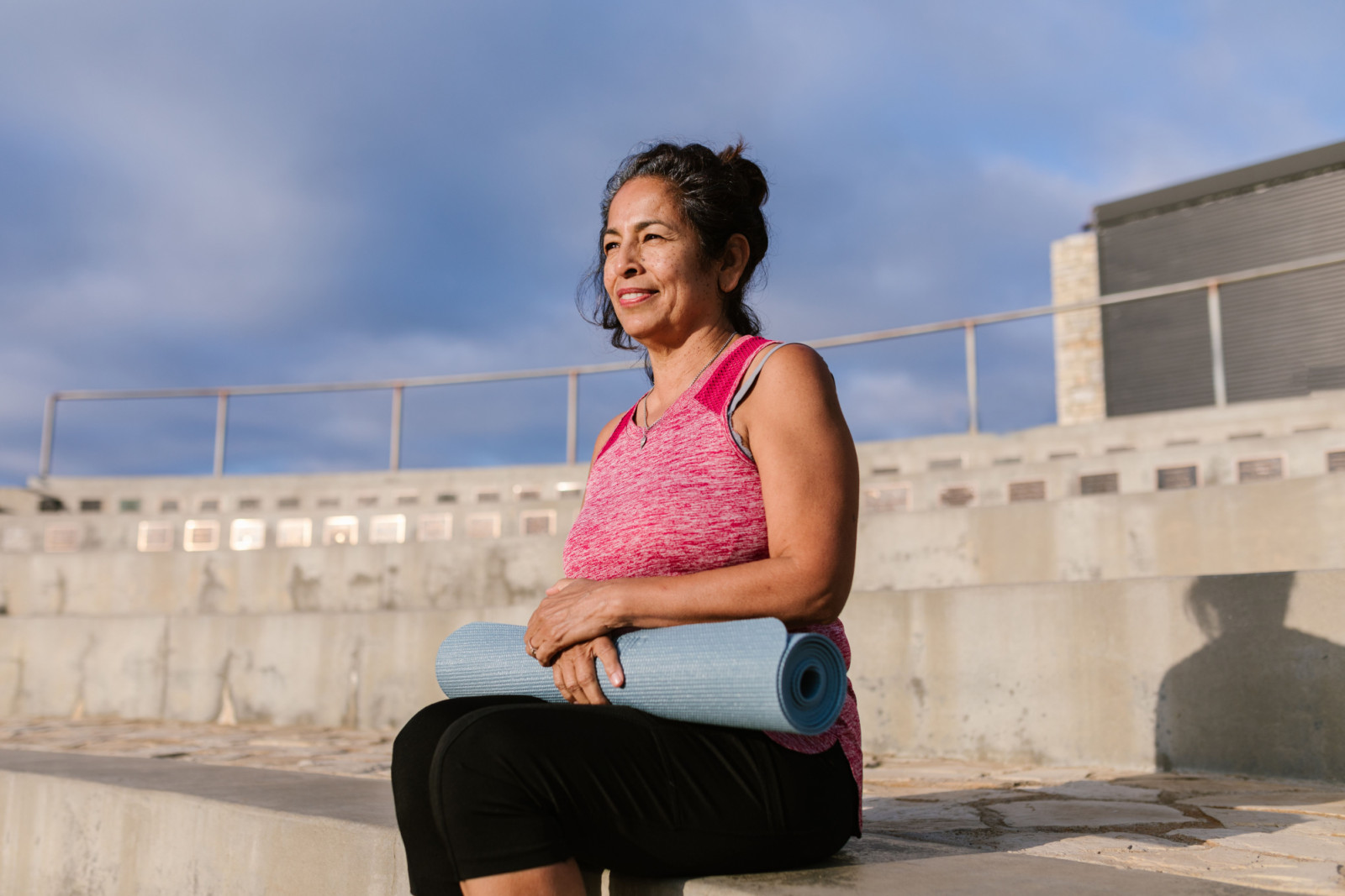 A woman with a yoga mat pauses outdoors, embracing practices that support a long, healthy life.
