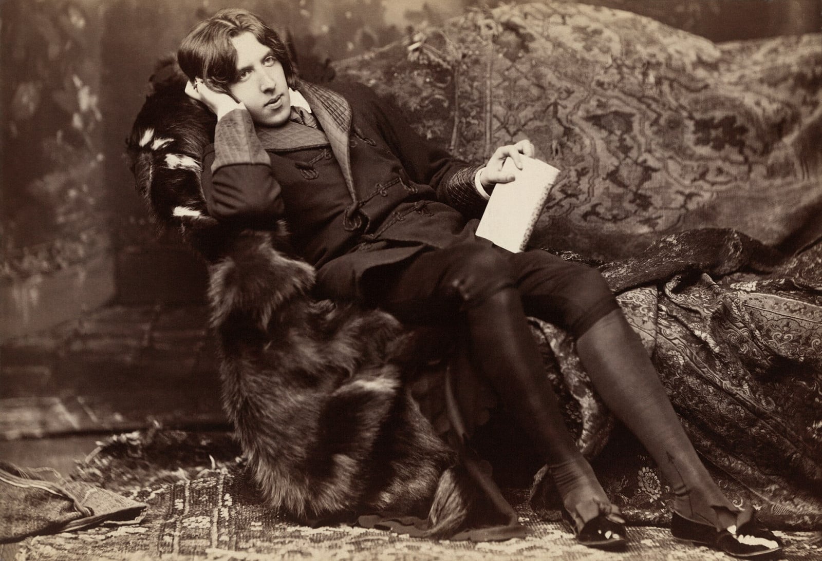 Oscar Wilde, the celebrated Irish playwright, poses with a book, embodying his literary brilliance.