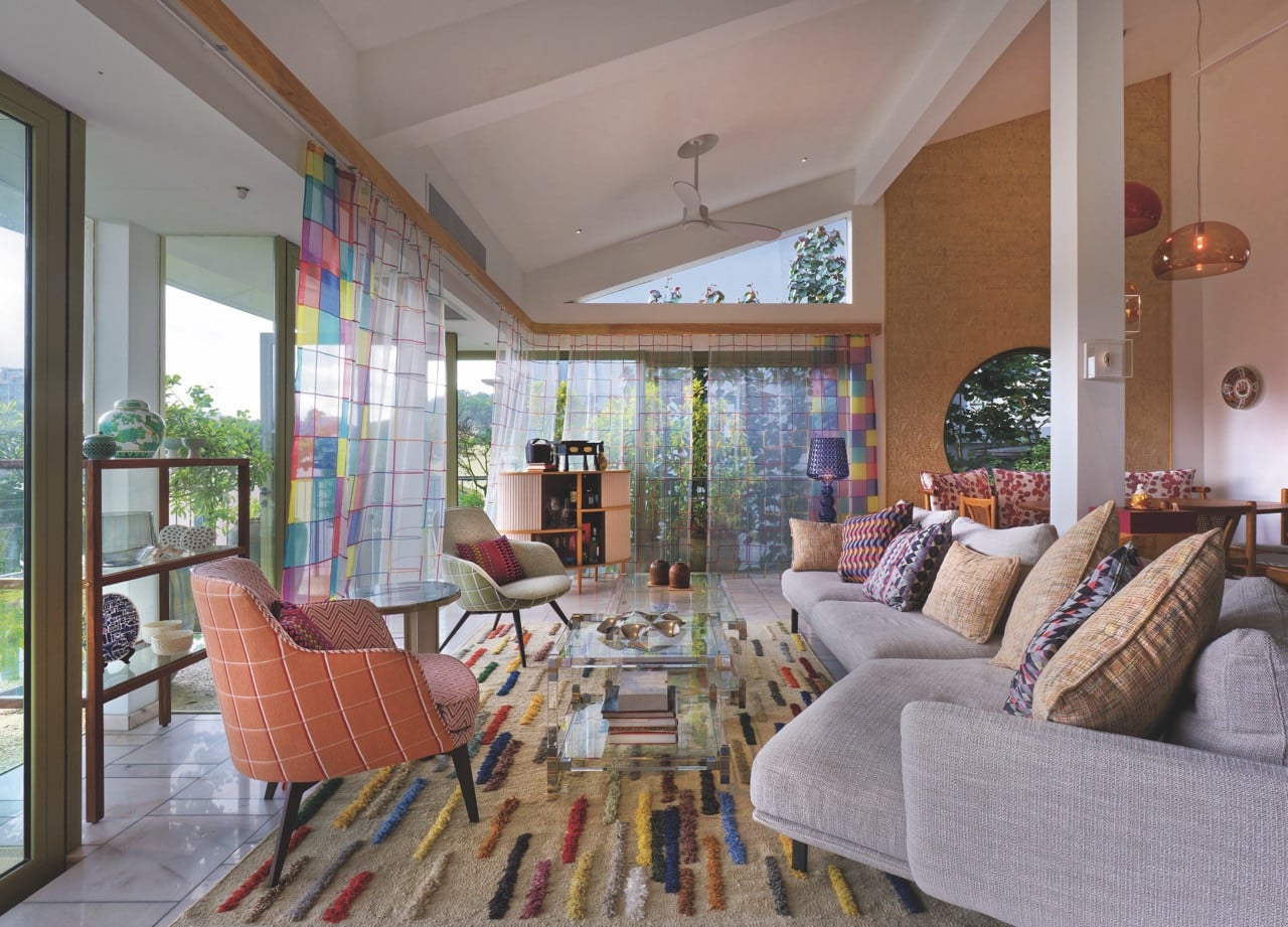 The top level’s open living and dining space, where a rainbow palette of curtain and cushion fabrics plays off neutral plaster walls and polished concrete