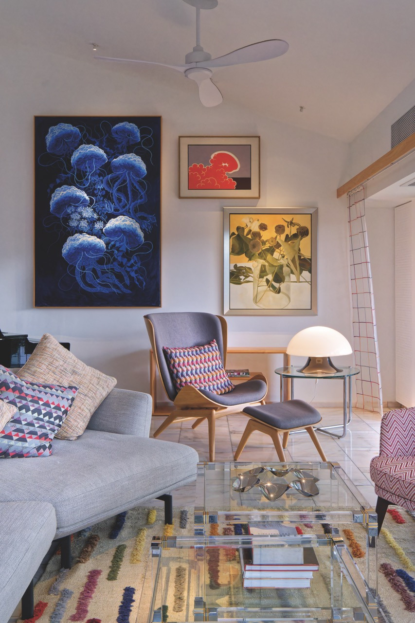 The high-ceilinged TV lounge takes on a gallery-like quality, with jewel-toned artwork and  a mix of vintage furniture against the neutral backdrop of white plaster