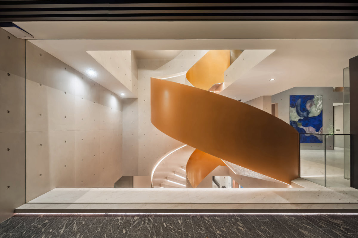 Finished in a champagne hue, the spiral staircase stands out against the fair-faced concrete walls
