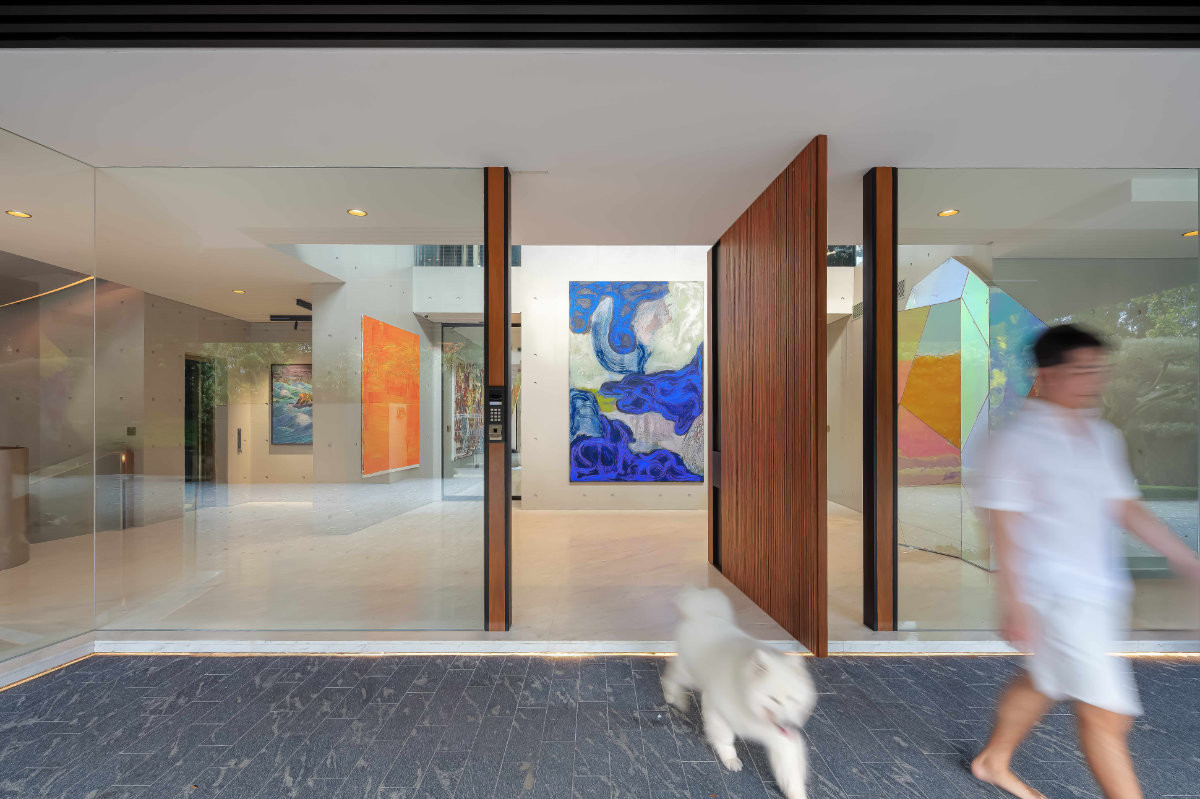 The gallery foyer is enclosed almost entirely in glass, with a timber pivot door providing a warm counterpoint to the transparent envelope.