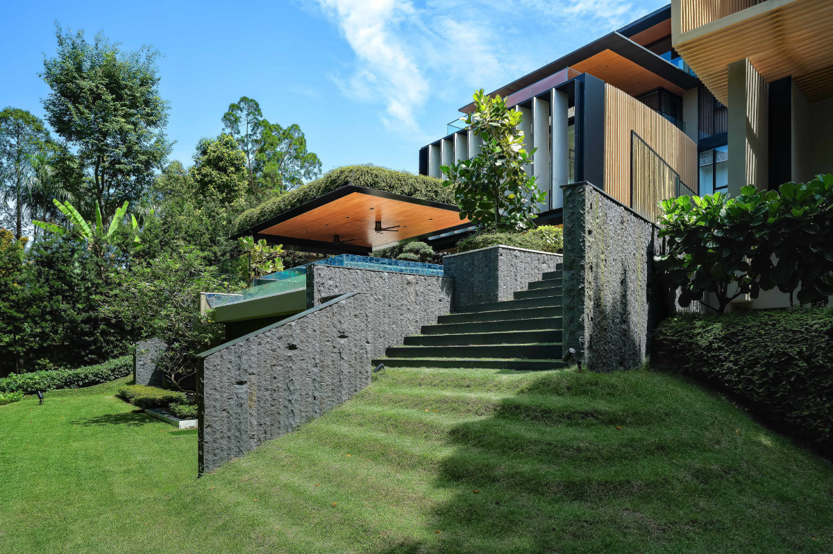 Terraced lawns and textured stone walls step up the slope towards the infinity pool and garden pavilion, showing how the house works with its steep site