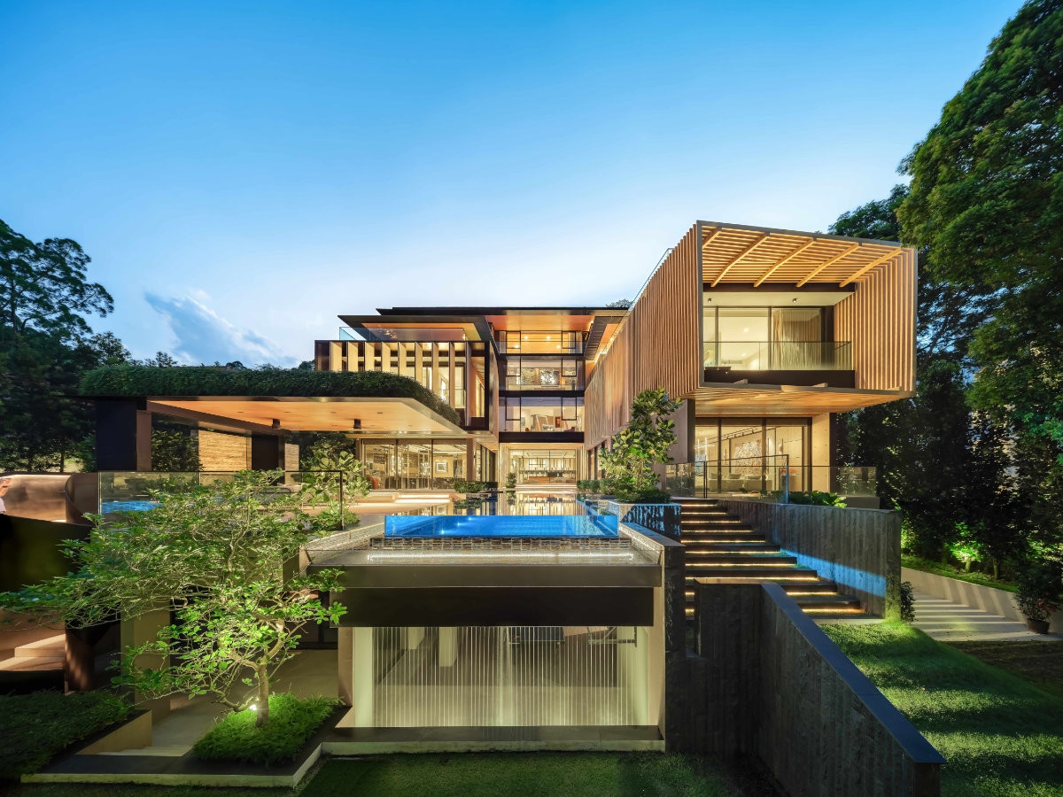 An evening view of this Good Class Bungalow in Bukit Timah by Lab Architects showcases the clever massing that hugs its steep, sloping site, resulting in five levels with access to natural light and greenery, and two wings with distinct framing as its visual language