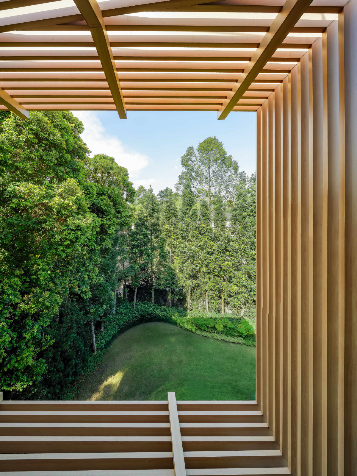 From inside the bedroom, the timber frame crops the sunken lawn and forest into a living picture