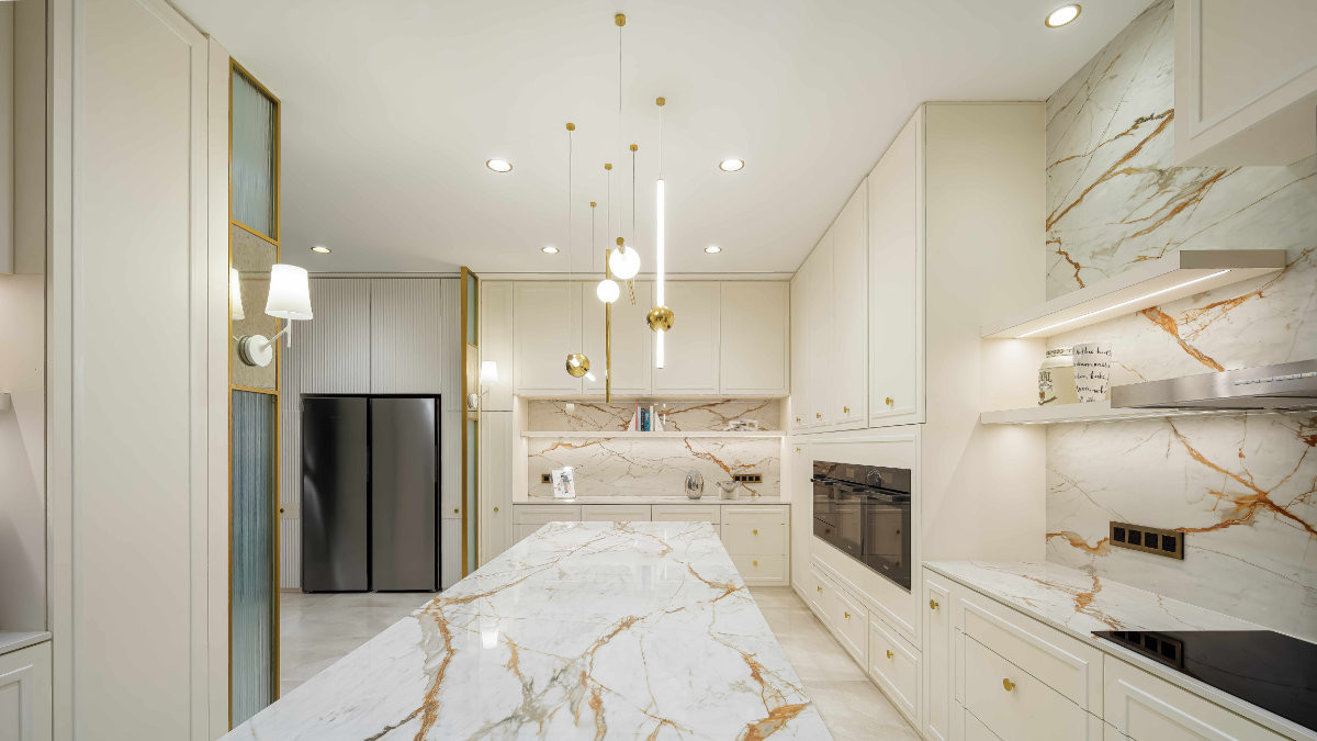 The kitchen pairs cream cabinetry and brass pendants with dramatically veined marble