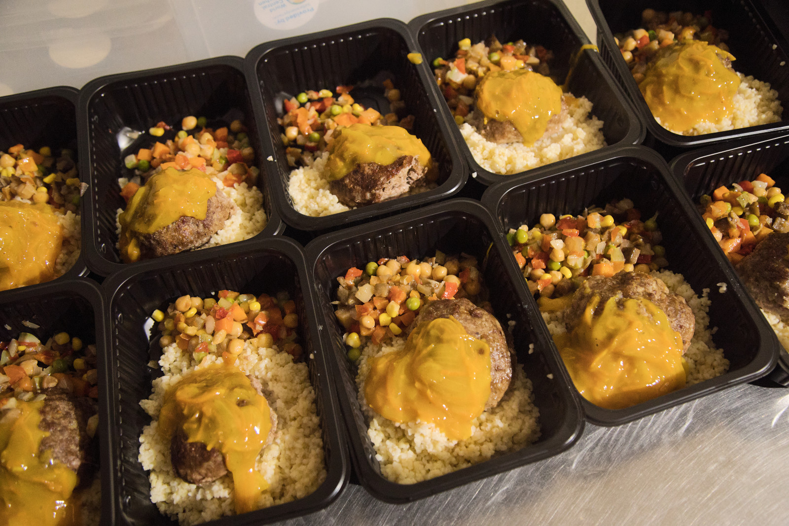 Individual portions of beef patties with a savory sauce, couscous, and diced vegetables, ready for a gourmet experience.