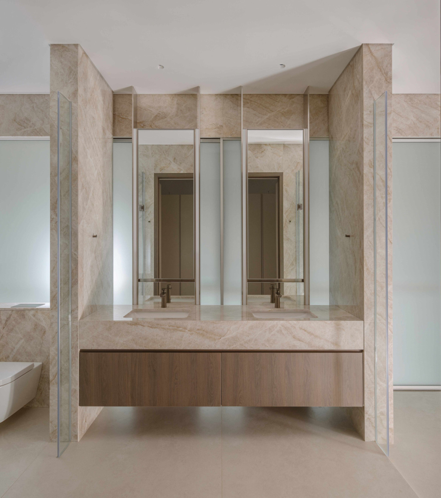 The double vanity’s tinted mirrors expand the marble-clad bathroom optically