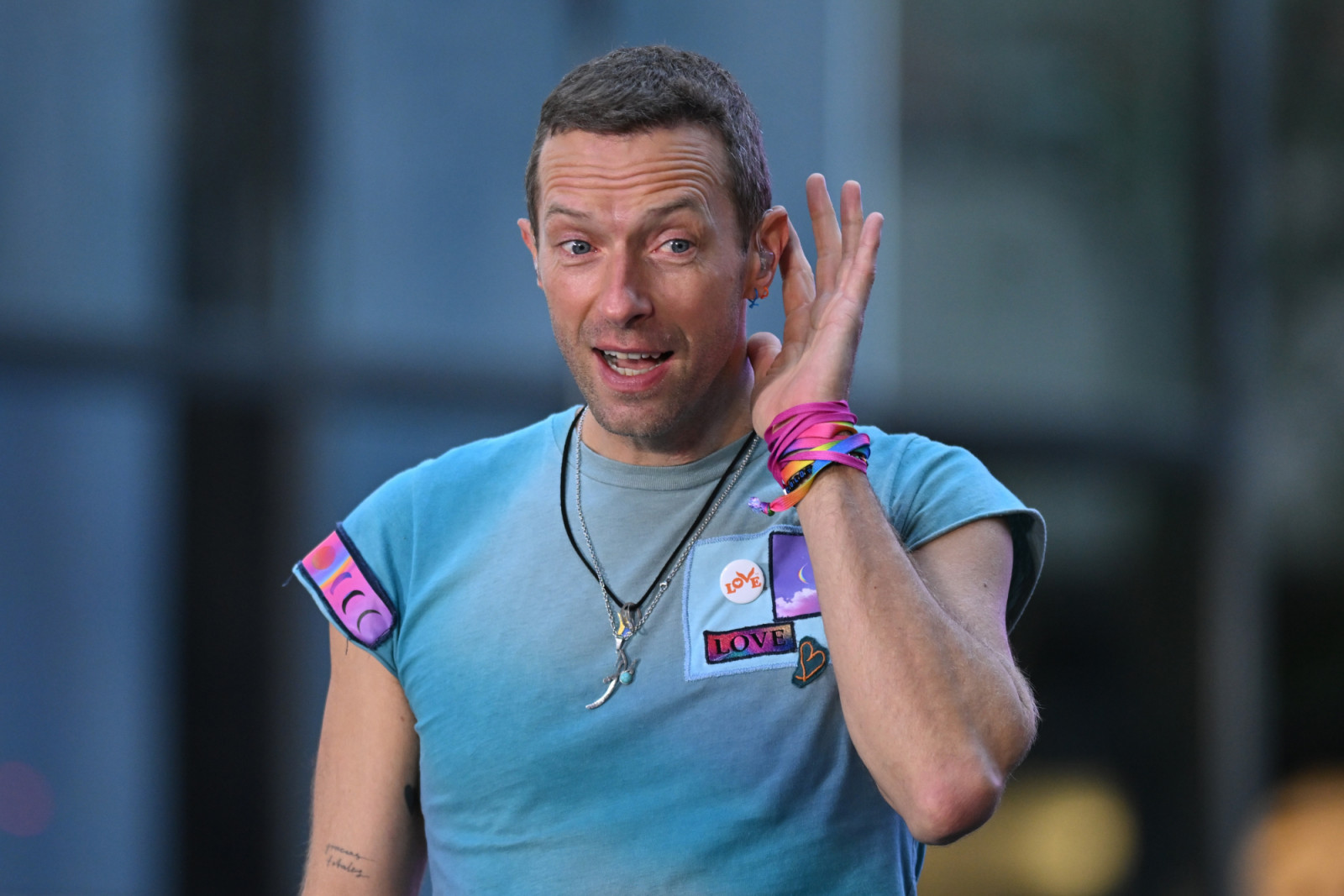 Chris Martin, lead singer of Coldplay, cups his ear while wearing an in-ear monitor.