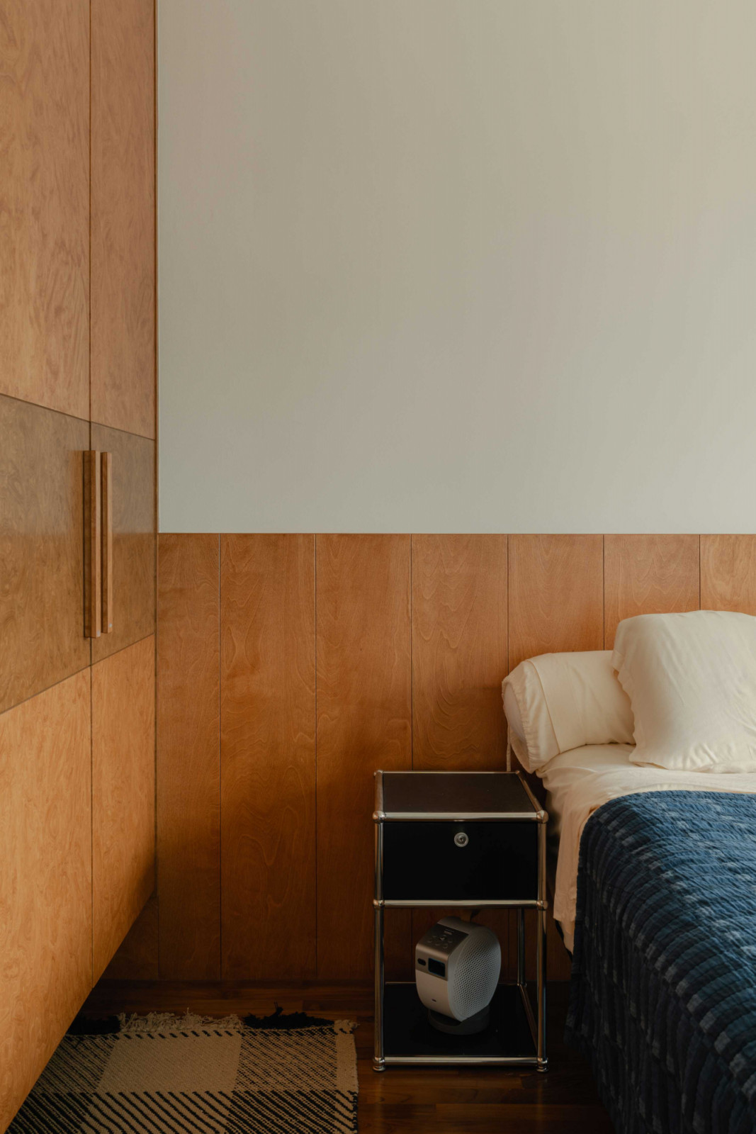 A steel bedside table offers contrast to the room’s warm wood panelling