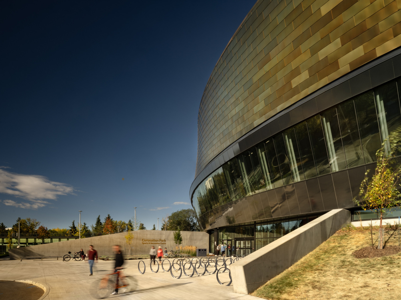 Bronze-toned metal panels clad the upper volume of the centre, which sits above a glazed band and a ground-floor entrance lined with bicycle racks (Photo: Nic Lehoux)
