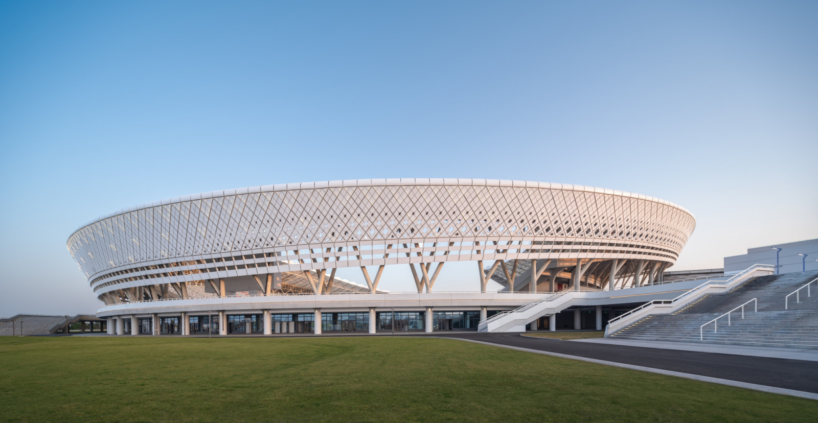 A diamond-patterned lattice wraps the outer face of the canopy, carried on branching columns above a podium with wide public staircases (Photo: Yilong Zhao)