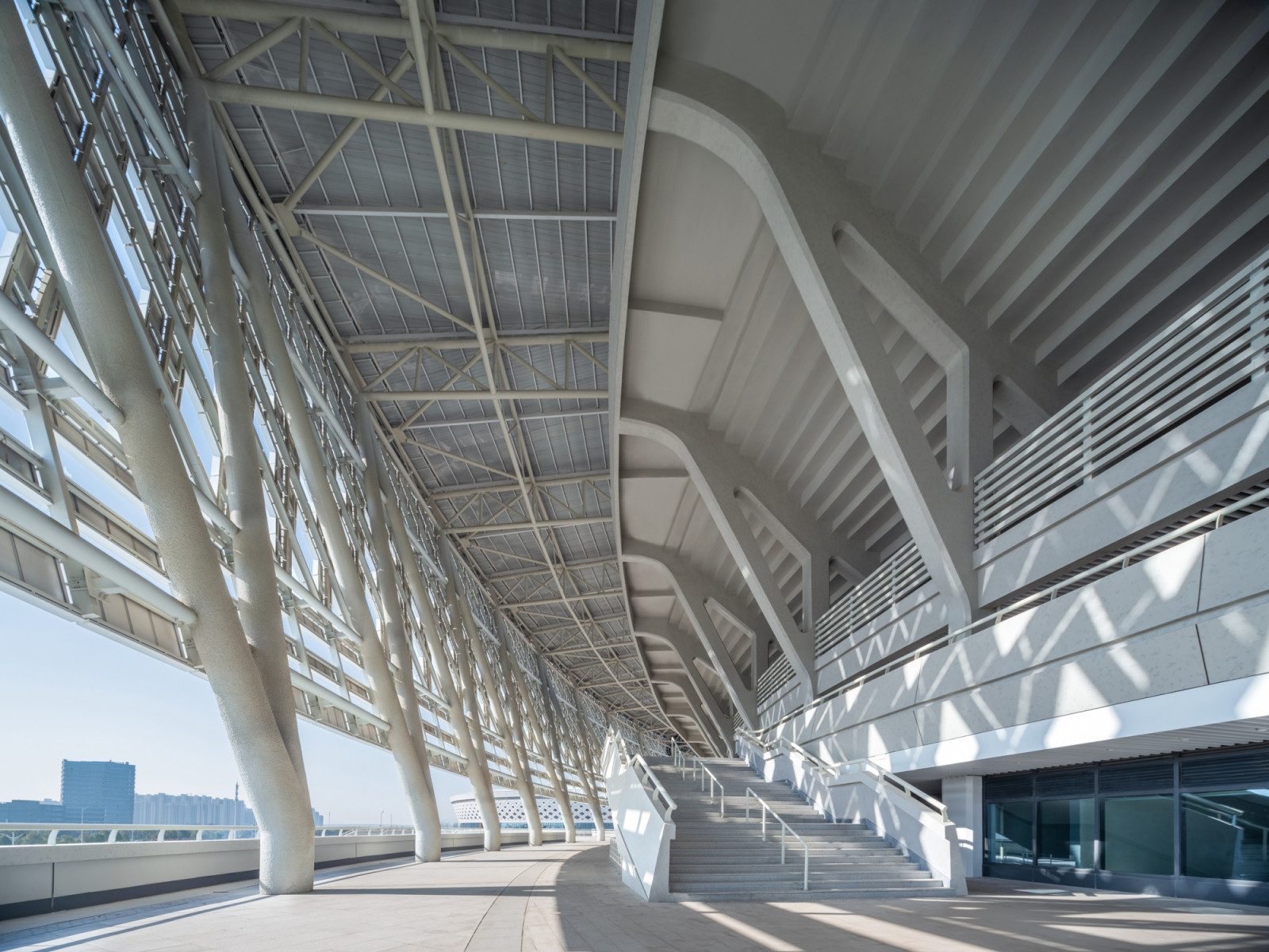 Inclined white columns and a steel roof truss frame the concourse beneath the canopy, where the lattice casts patterned shadows across the floor (Photo: Yilong Zhao)