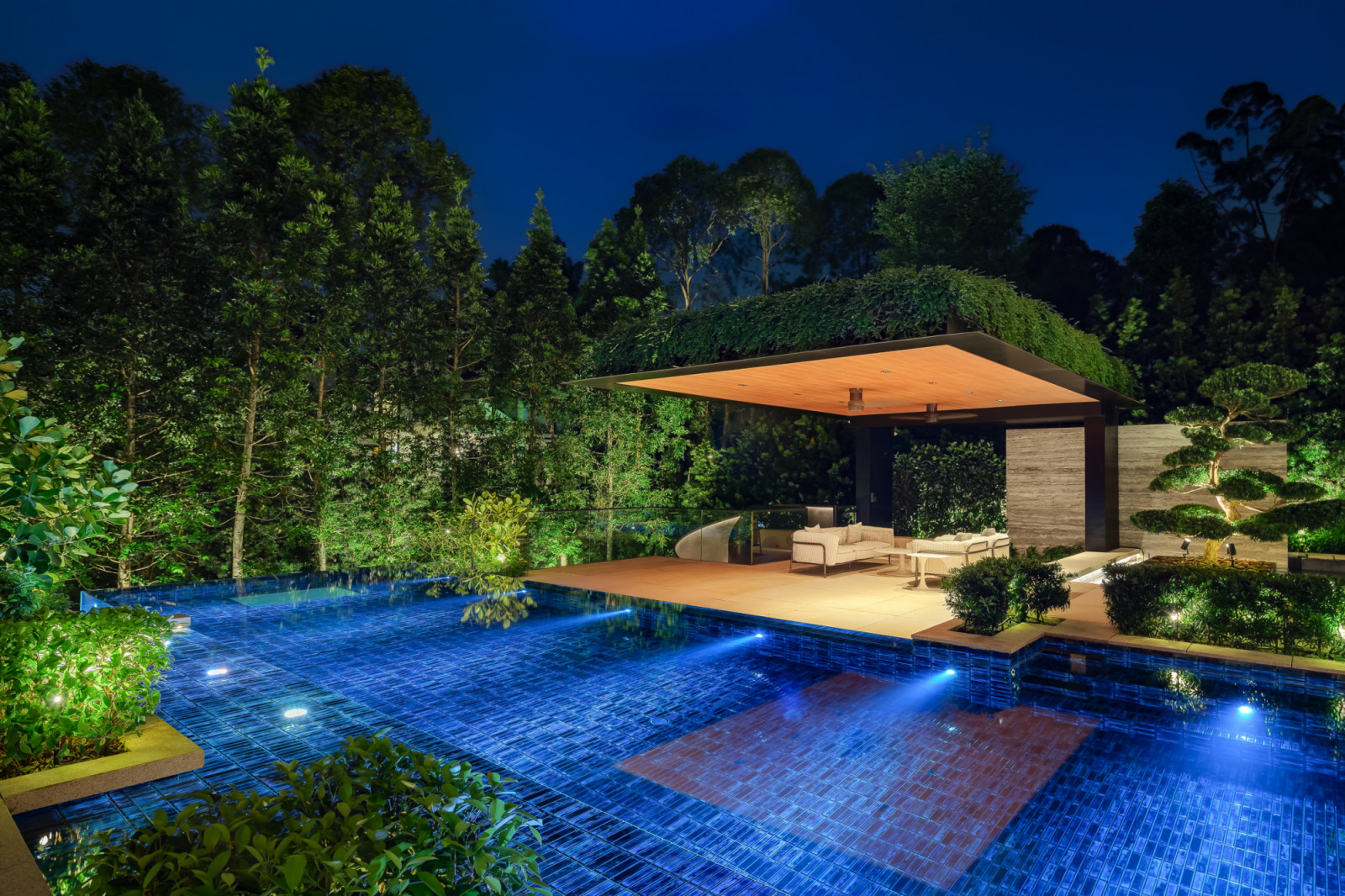 At night, the planted garden pavilion glows beside the infinity pool