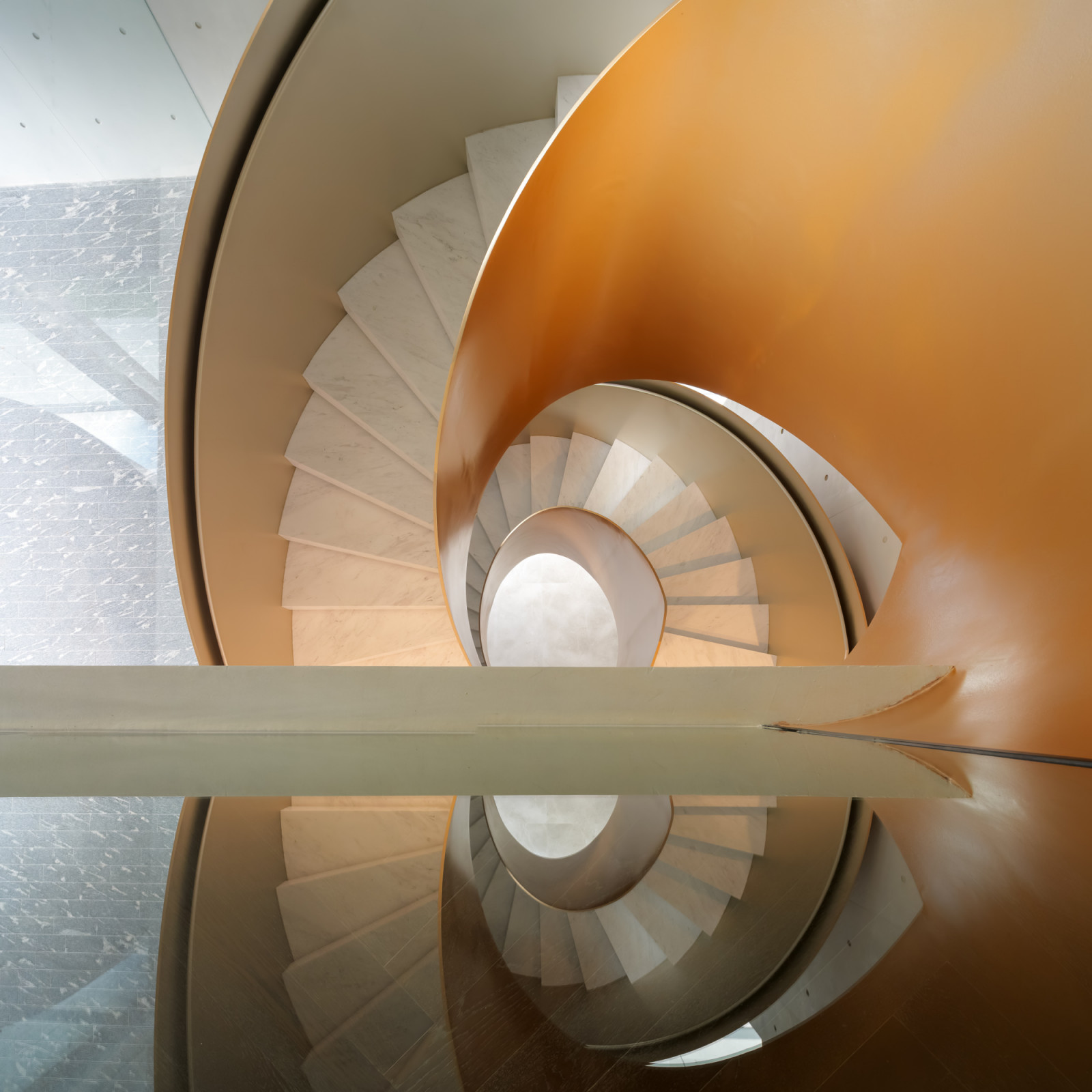 The spiral staircase’s champagne casing and marble treads doubled in a glass reflection