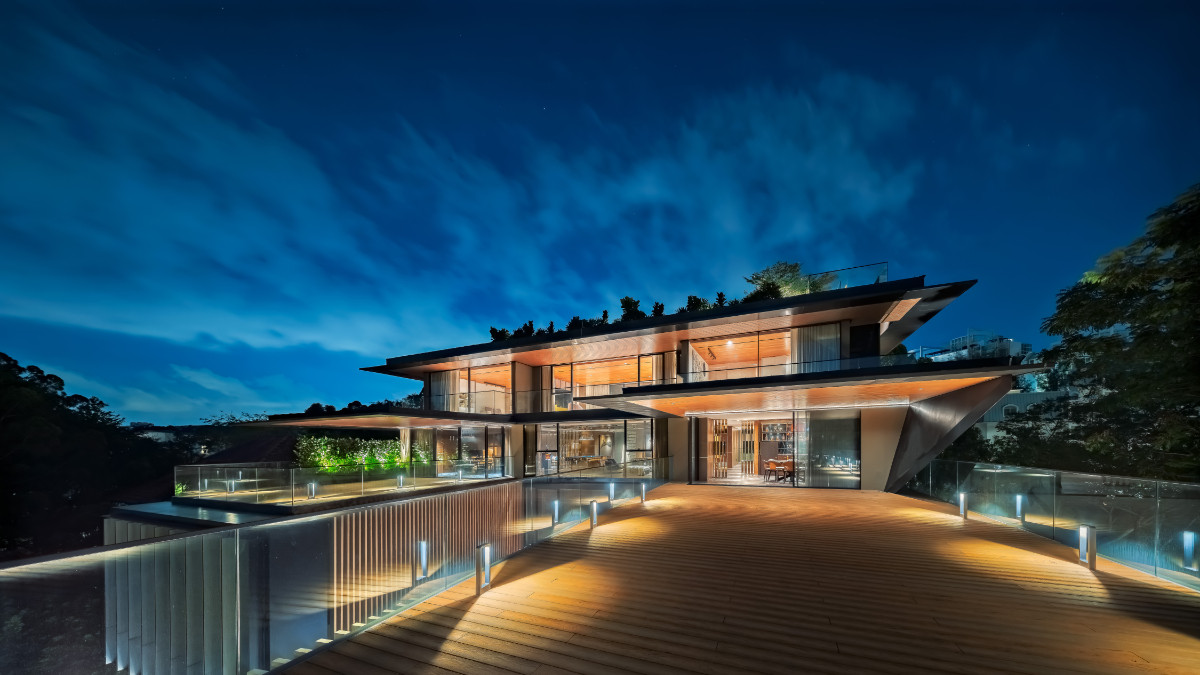At night, the upper levels glow beneath layered cantilevered roofs, seen from the expansive timber-decked terrace