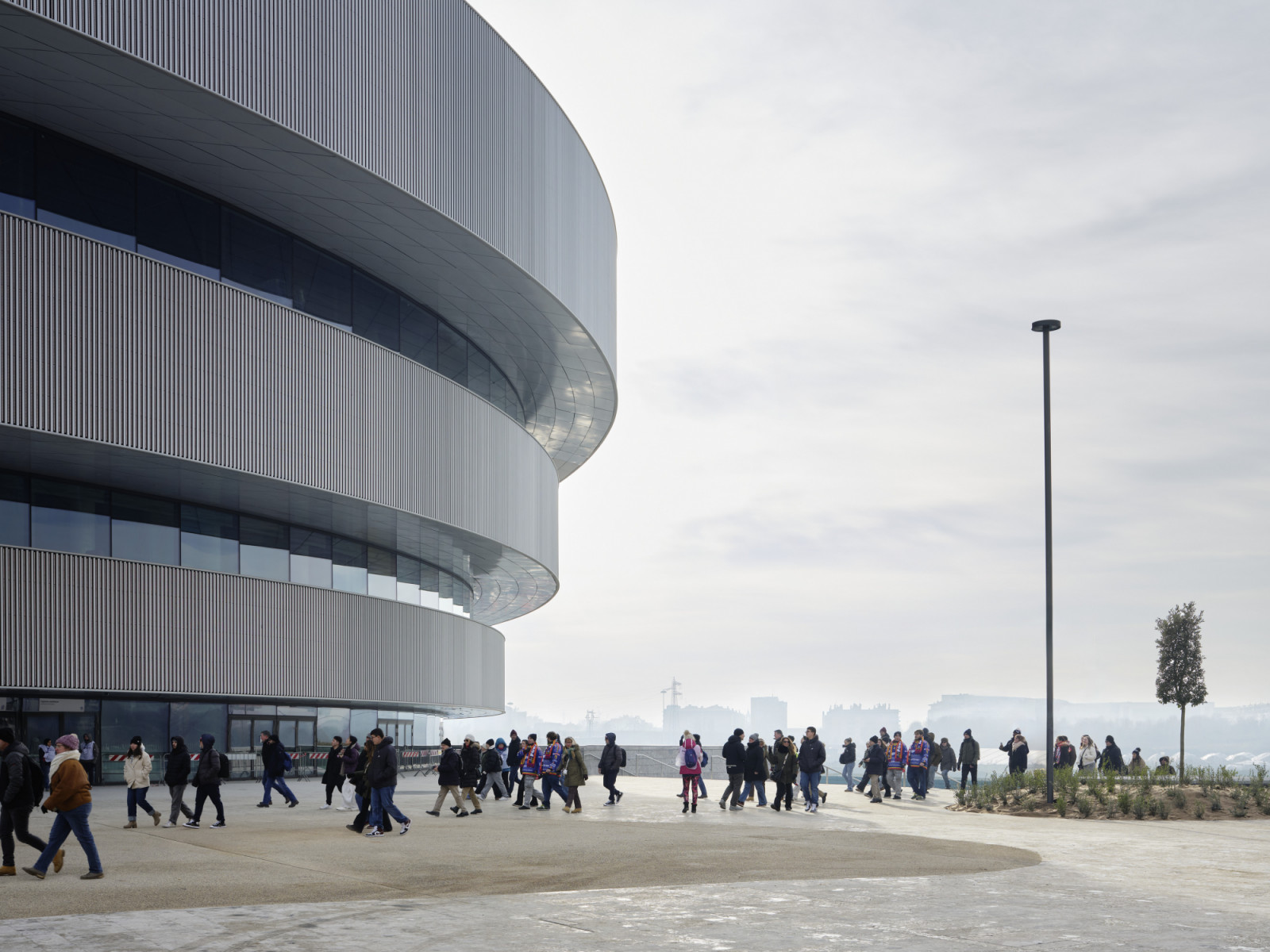 Visitors cross the forecourt beneath the Unipol Dome’s three rings, whose aluminium tubes alternate with bands of glazing (Photo: Noshe)