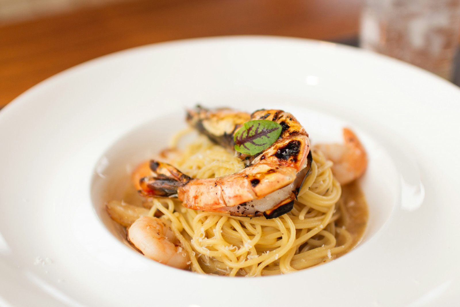 Spaghetti with grilled prawns, adorned with Parmesan and a fresh herb garnish.
