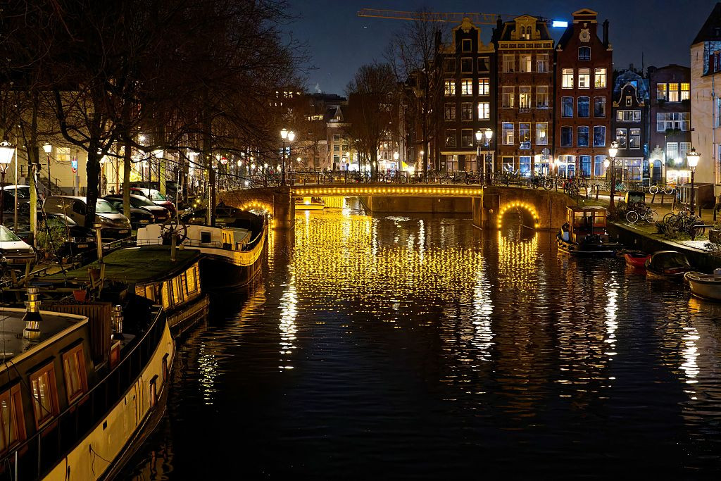 Soft Lights Reflect Off A Calm Canal In Amsterdam At Night. Boats Line The Waterway. While Historic Buildings Create A Picturesque Backdrop For The Serene Winter Atmosphere. Amsterdam. Netherlands. Europe. (Photo by: Paolo Reda/REDA/Universal Images Group via Getty Images)